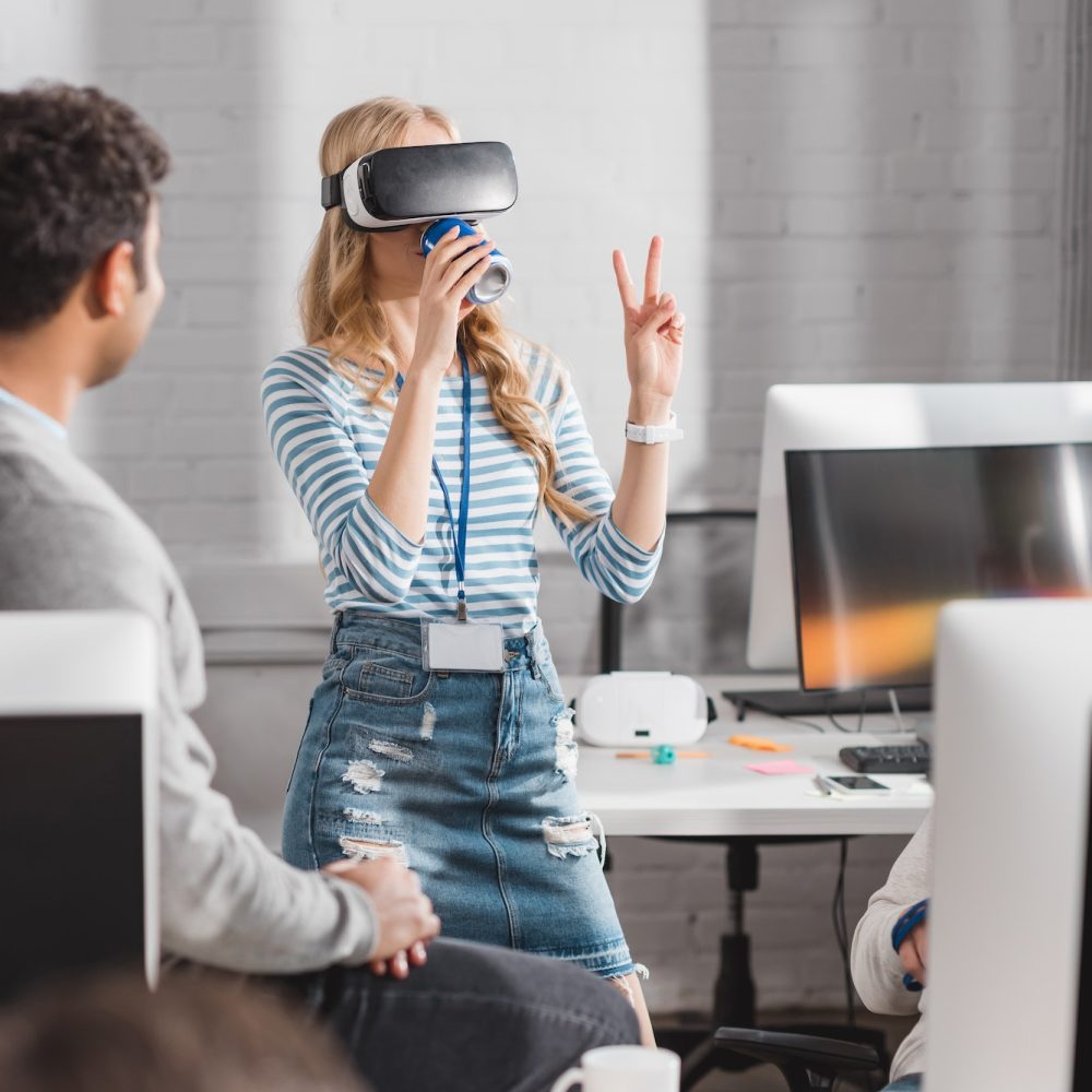 young woman drinking beverage in virtual reality glasses at modern office